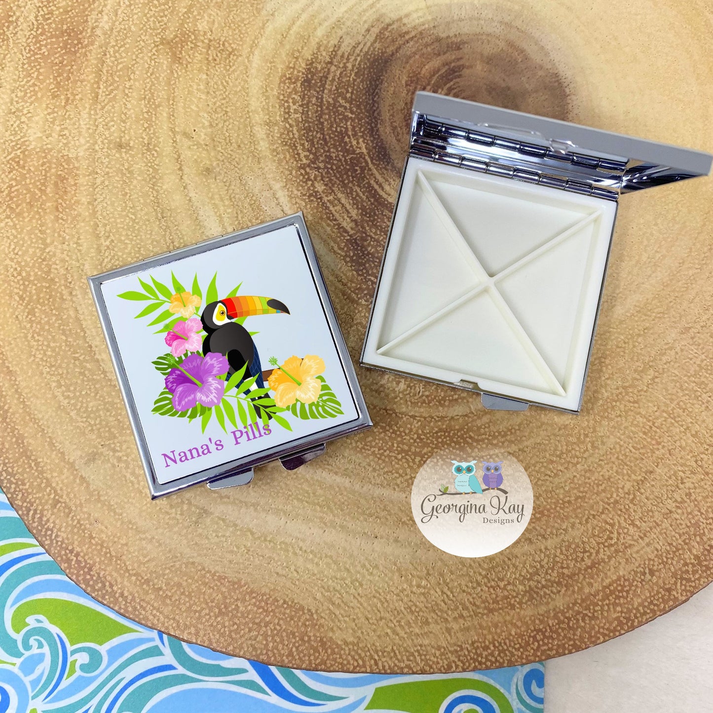 Compact mirror with toucan design on a wooden surface, featuring the brand 'Georgina Kay Designs Co'.