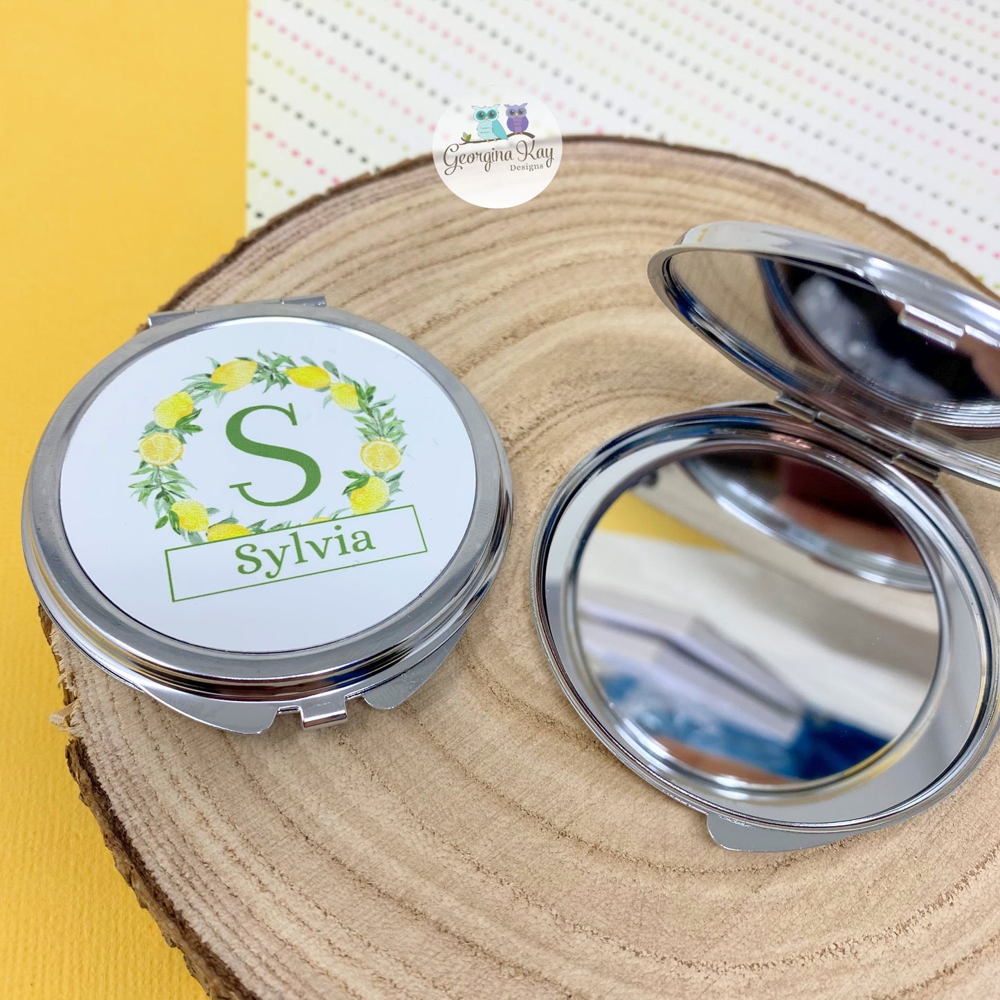 Compact mirror with 'Sylvia' design on a wooden surface