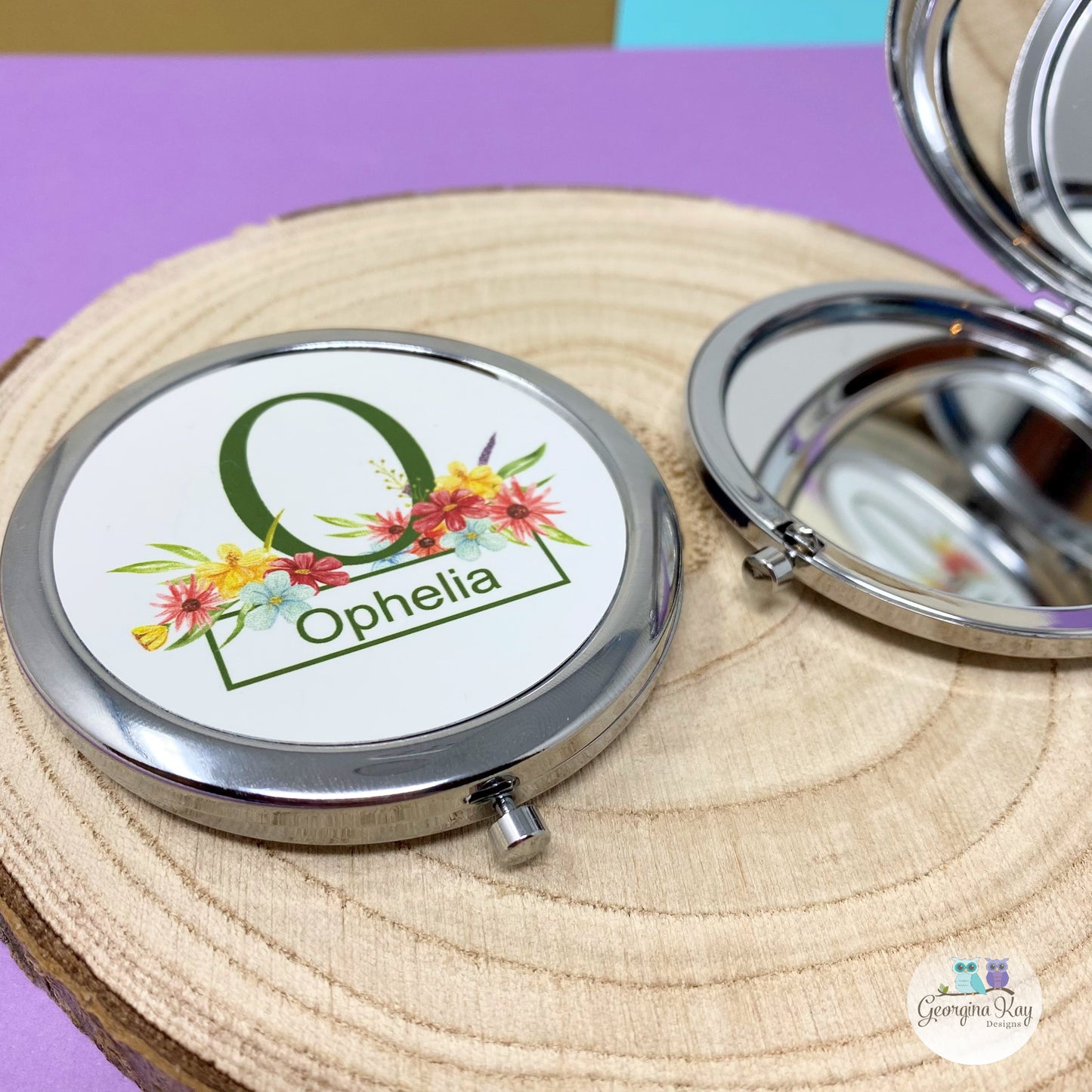 Compact mirror with floral design and 'Ophelia' text on a wooden surface