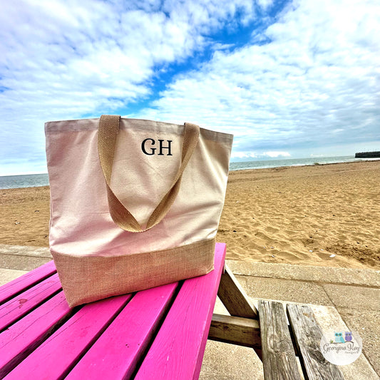 Beige tote bag with 'GH' monogram on a pink table at the beach
