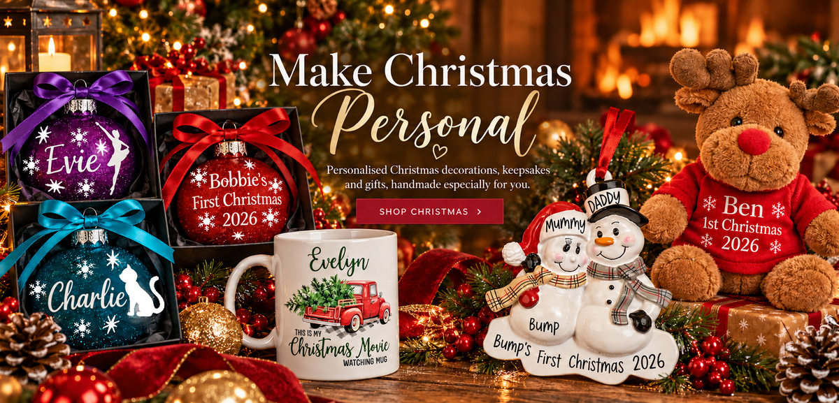 A festive Christmas-themed promotional banner with multiple personalized ornaments, mugs, a teddy bear, and holiday decorations. Large text reads 'Make Christmas Personal' with smaller copy about personalized Christmas decorations, keepsakes, and gifts, and a red button that says 'SHOP CHRISTMAS'.