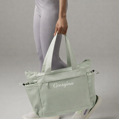 Person holding a light green tote bag with 'Georgina' branding on a gray background