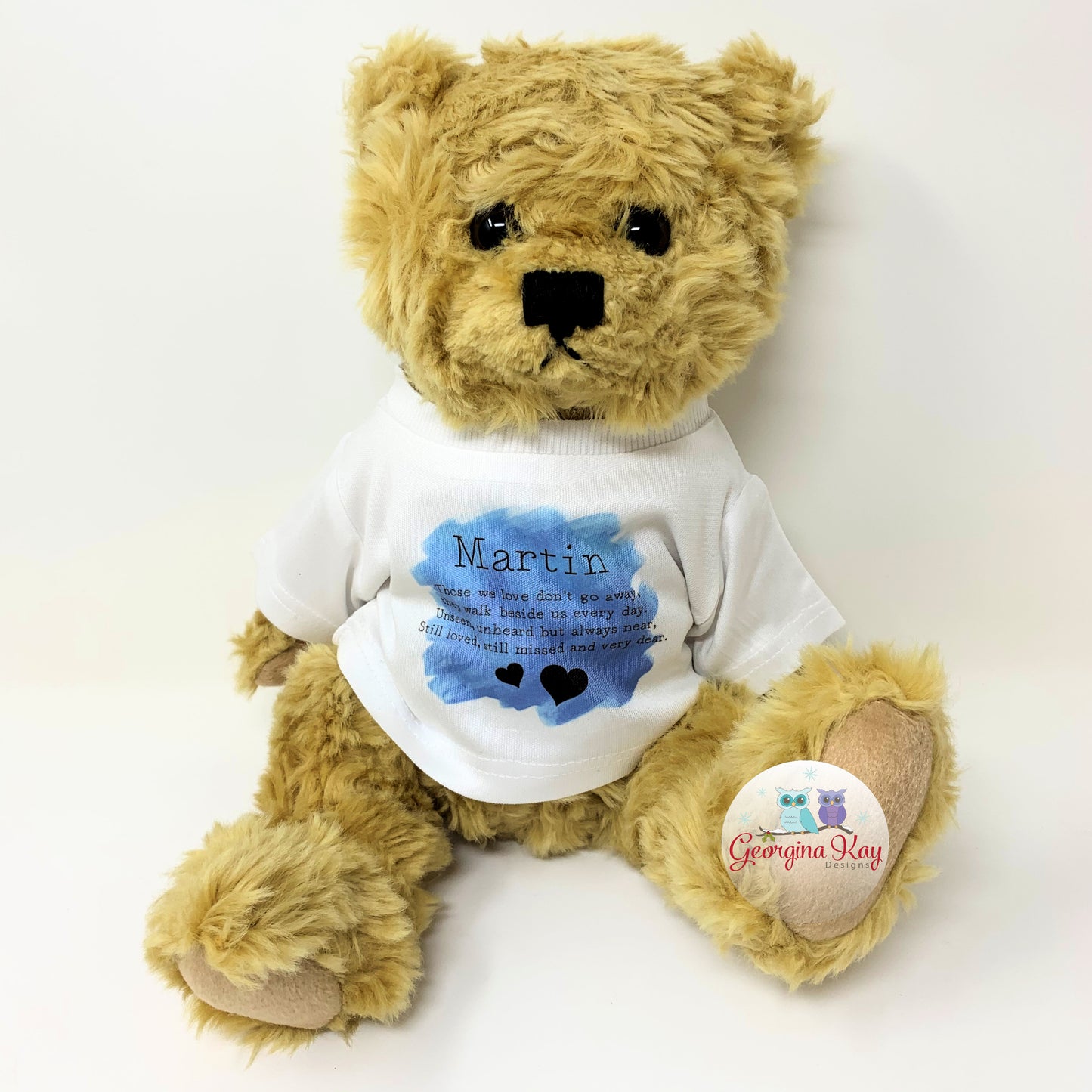 Teddy bear wearing a white shirt with text and a blue heart, on a white background.