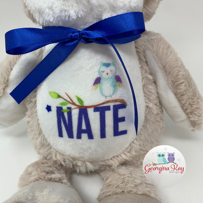 Stuffed animal with a blue ribbon and 'NATE' embroidered on a white background, featuring the Georgina kay Design logo.