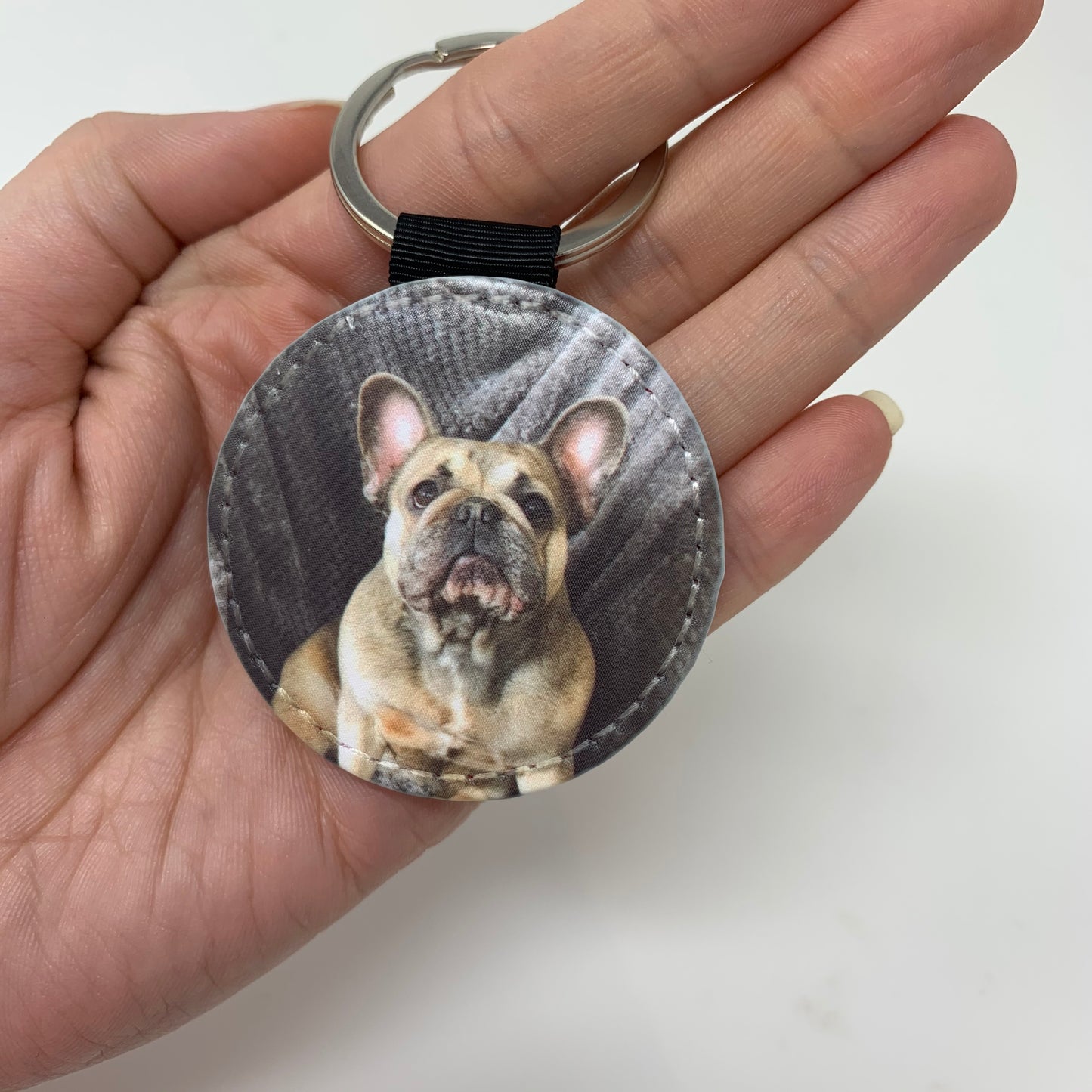 Round key fob with a dog design held in a hand against a plain background