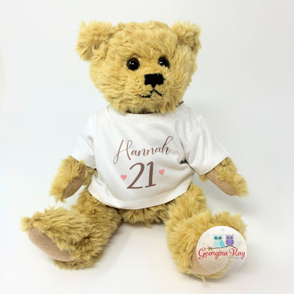 Teddy bear wearing a white shirt with 'Hannah 21' printed on it, on a white background.