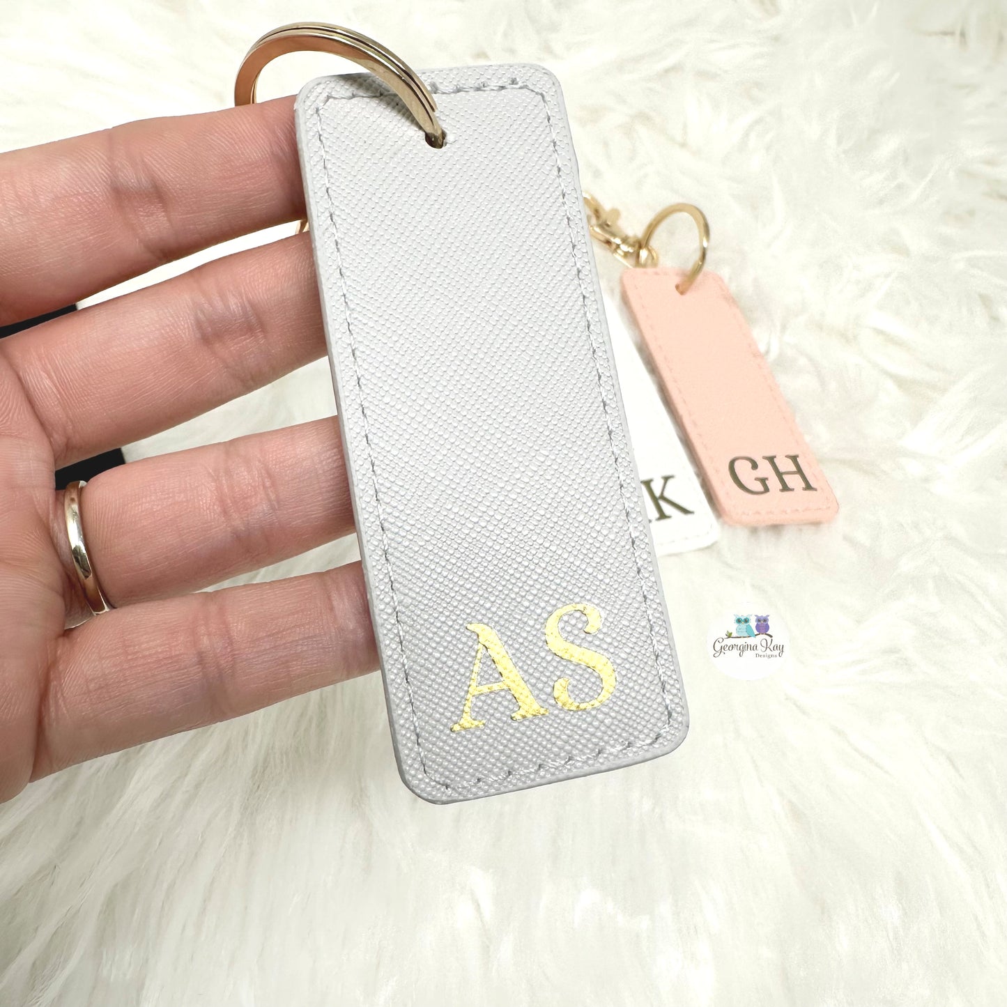 White keychain with gold initials held by a hand on a white background