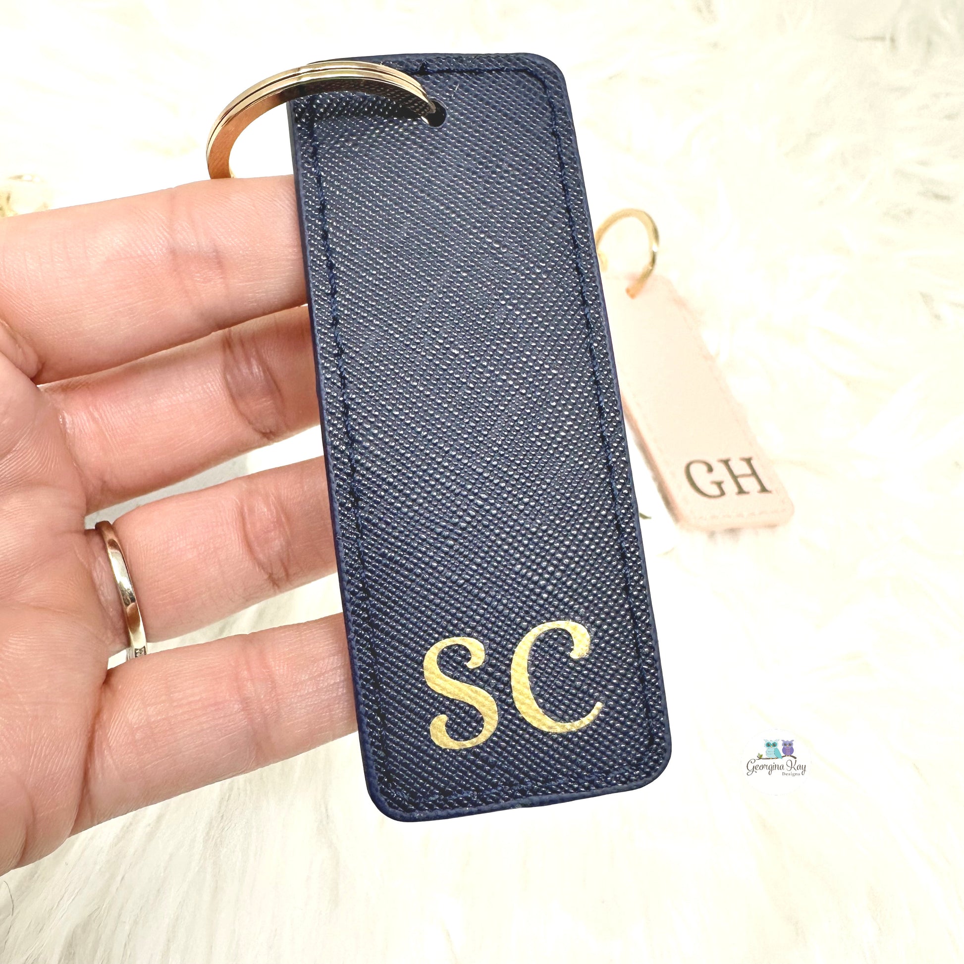Navy keychain with gold initials held by a hand on a light background
