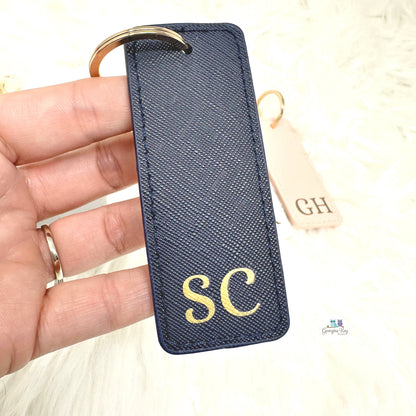 Navy keychain with gold initials held by a hand on a light background