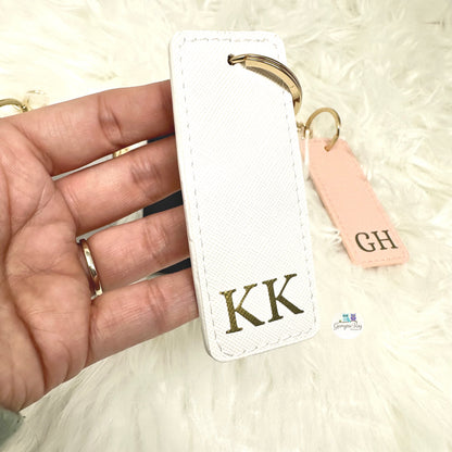 White keychain with gold letters 'KK' held by a hand on a light background