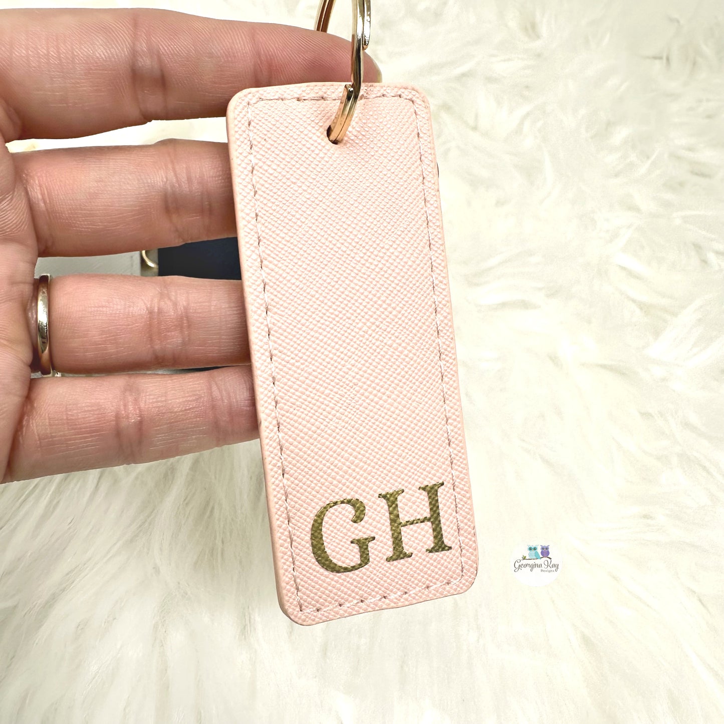 Pink keychain with 'GH' initials held by a hand on a white background
