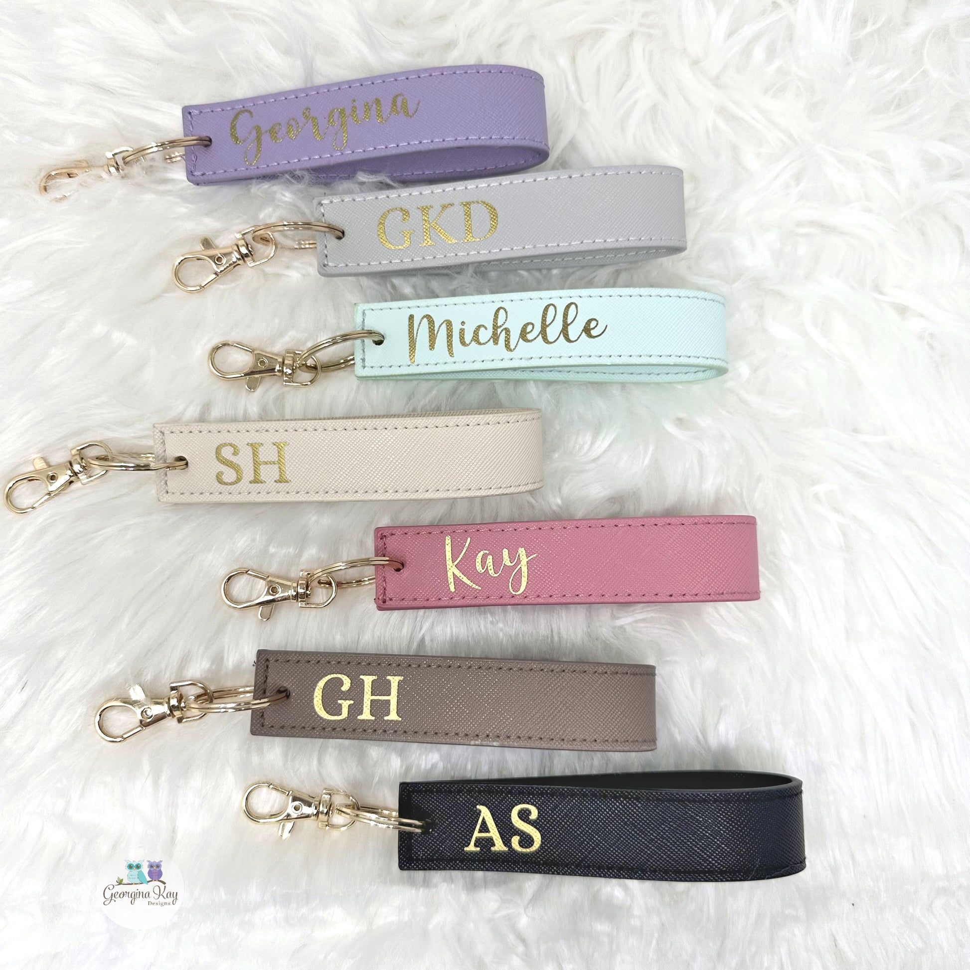 Personalized keychains with names in gold on various pastel-colored straps.