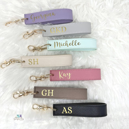 Personalized keychains with names in gold on various pastel-colored straps.