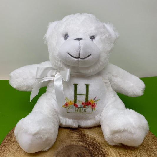 White teddy bear with a ribbon and embroidered name on a wooden surface