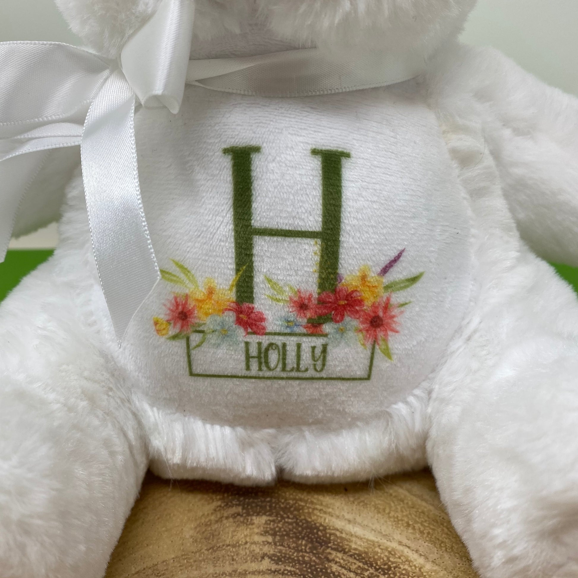 White teddy bear with 'H' and 'Holly' embroidery on a wooden surface