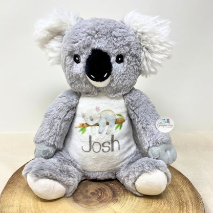 Plush koala toy with a white shirt displaying an illustration and the name 'Josh' on a wooden surface.