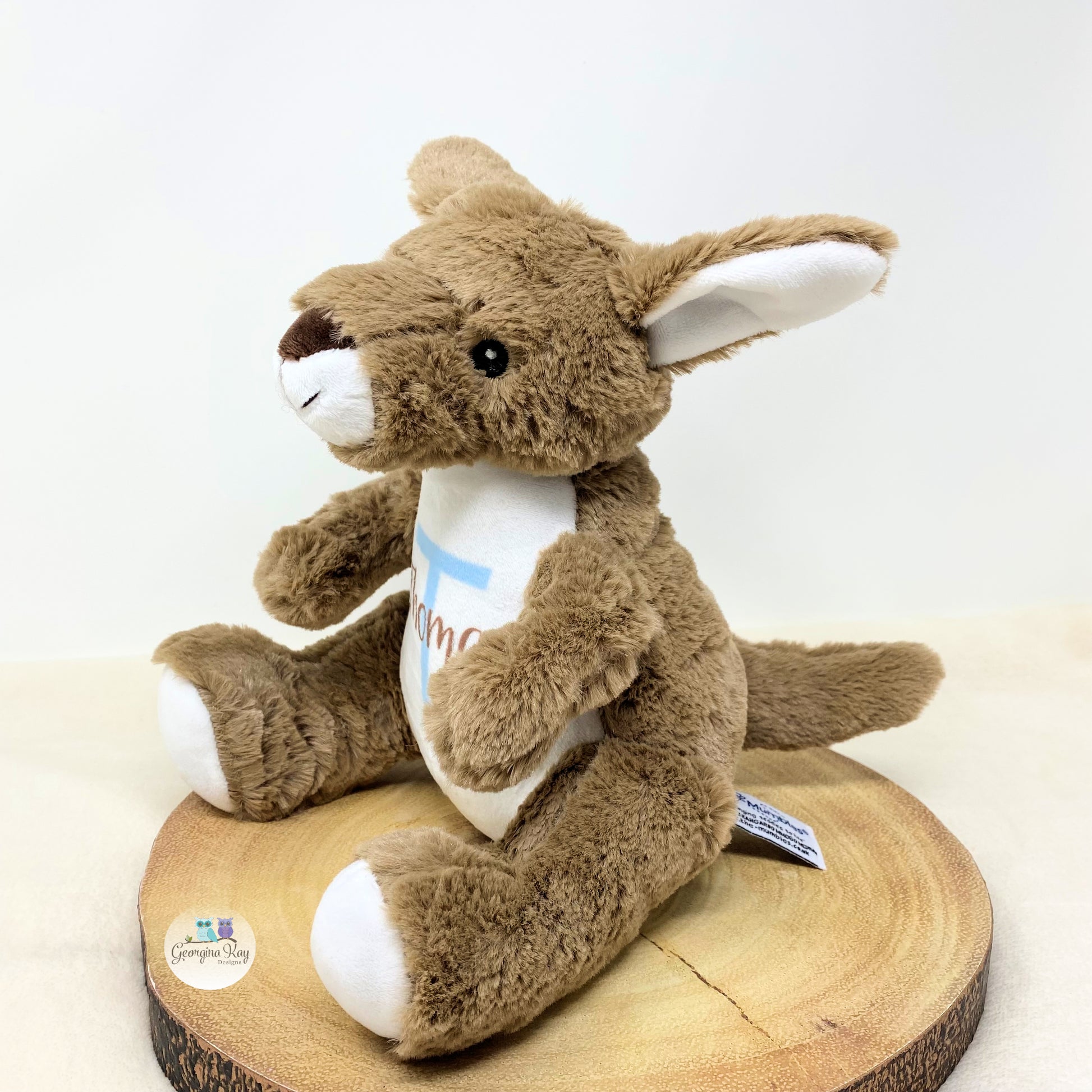 Plush kangaroo toy sitting on a wooden log with a white background