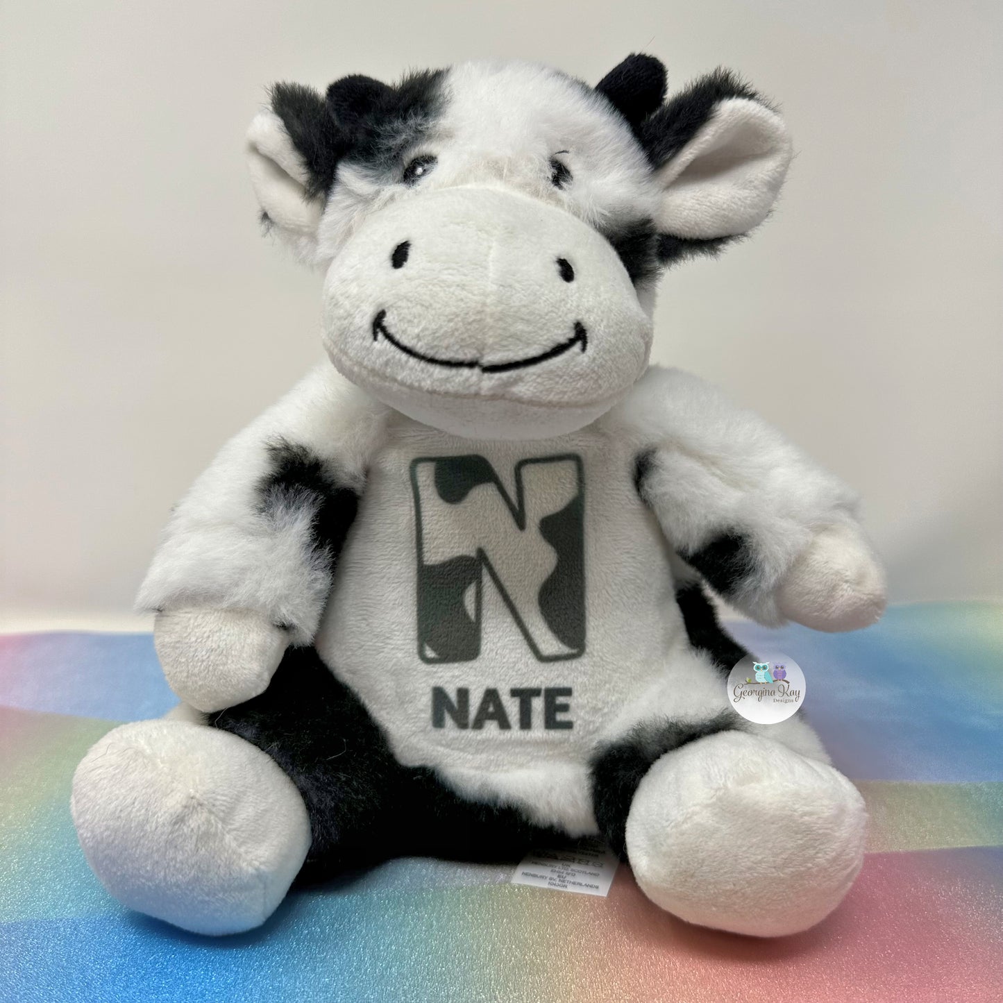 Plush cow toy with 'Nate' on a colorful surface