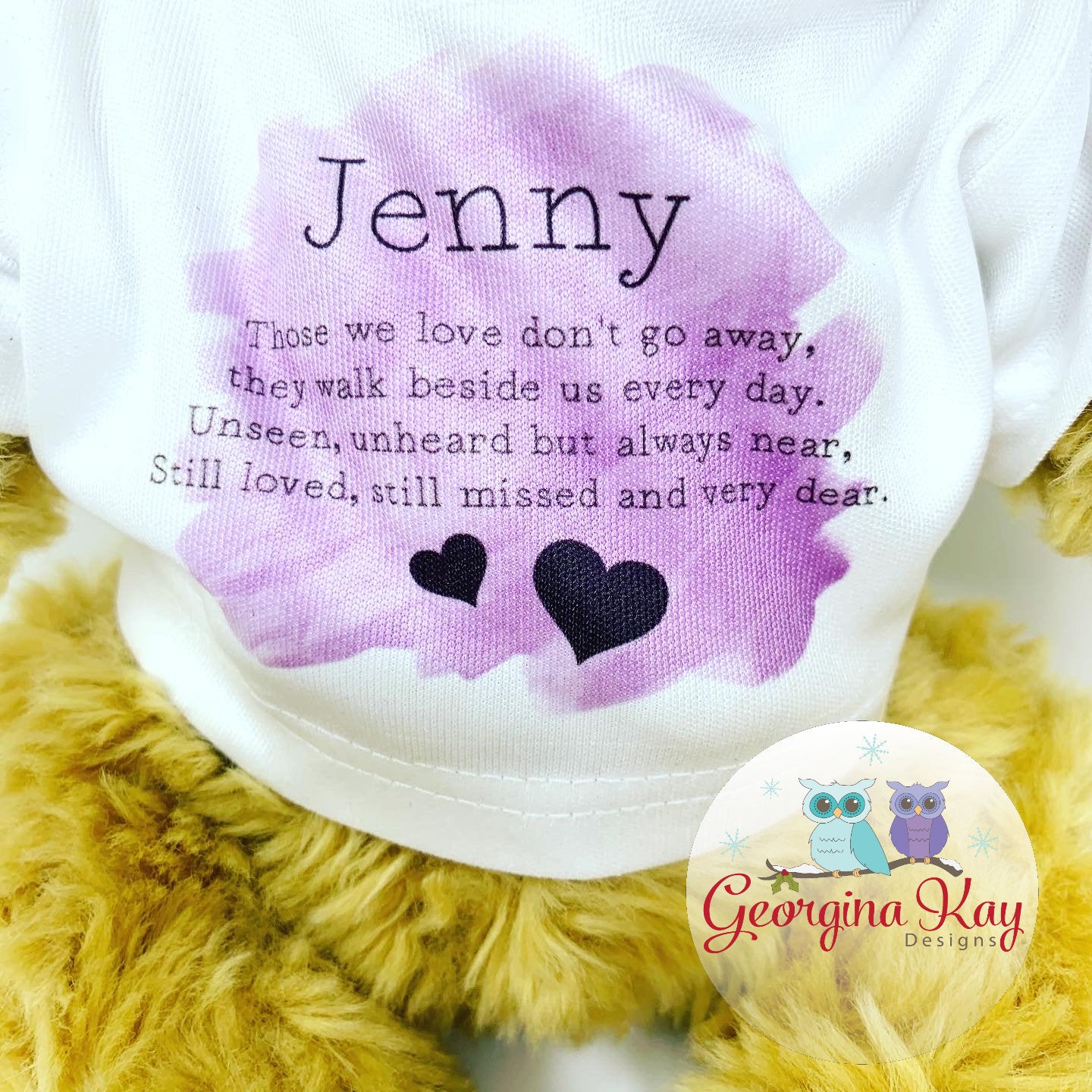 Plush toy with a purple heart-shaped patch featuring text and 'Georgina Kay Designs' logo.
