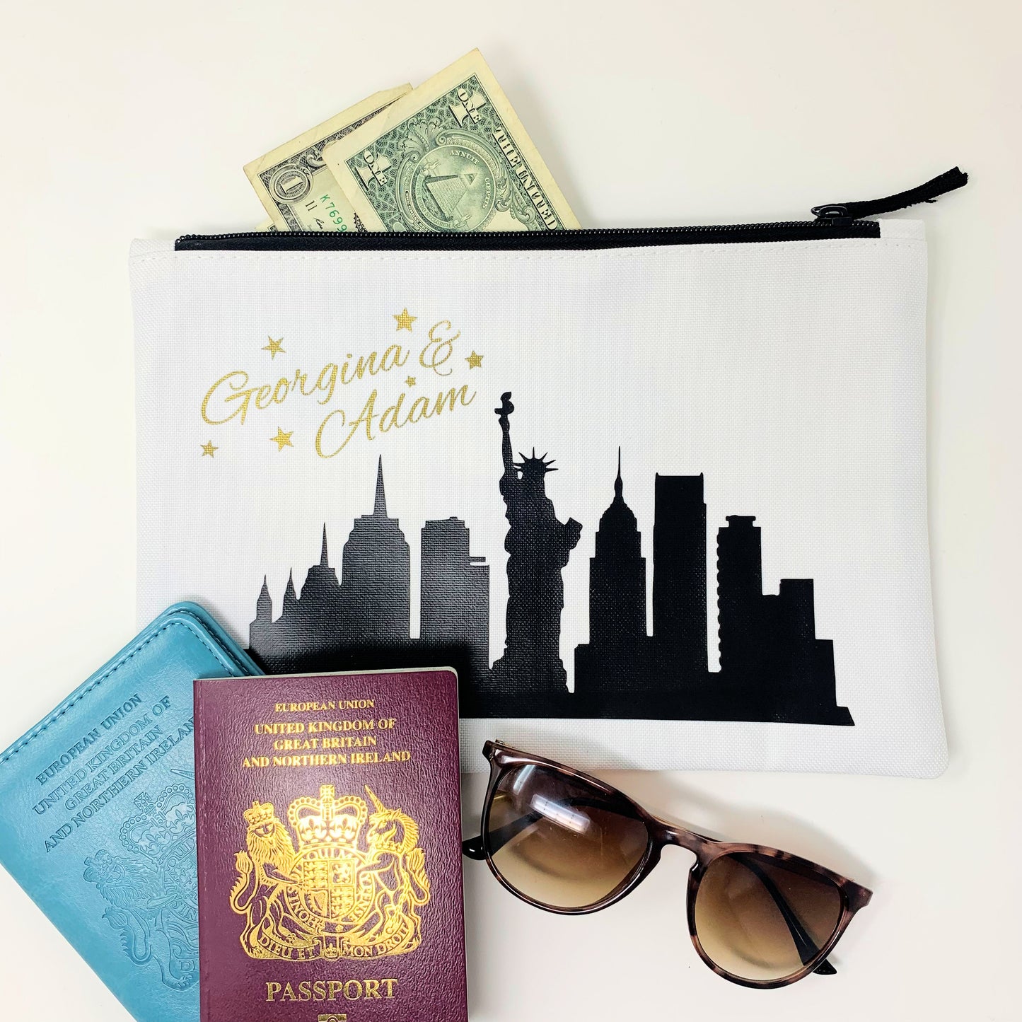 Pouch with a city skyline design, passport, sunglasses, and money on a white background