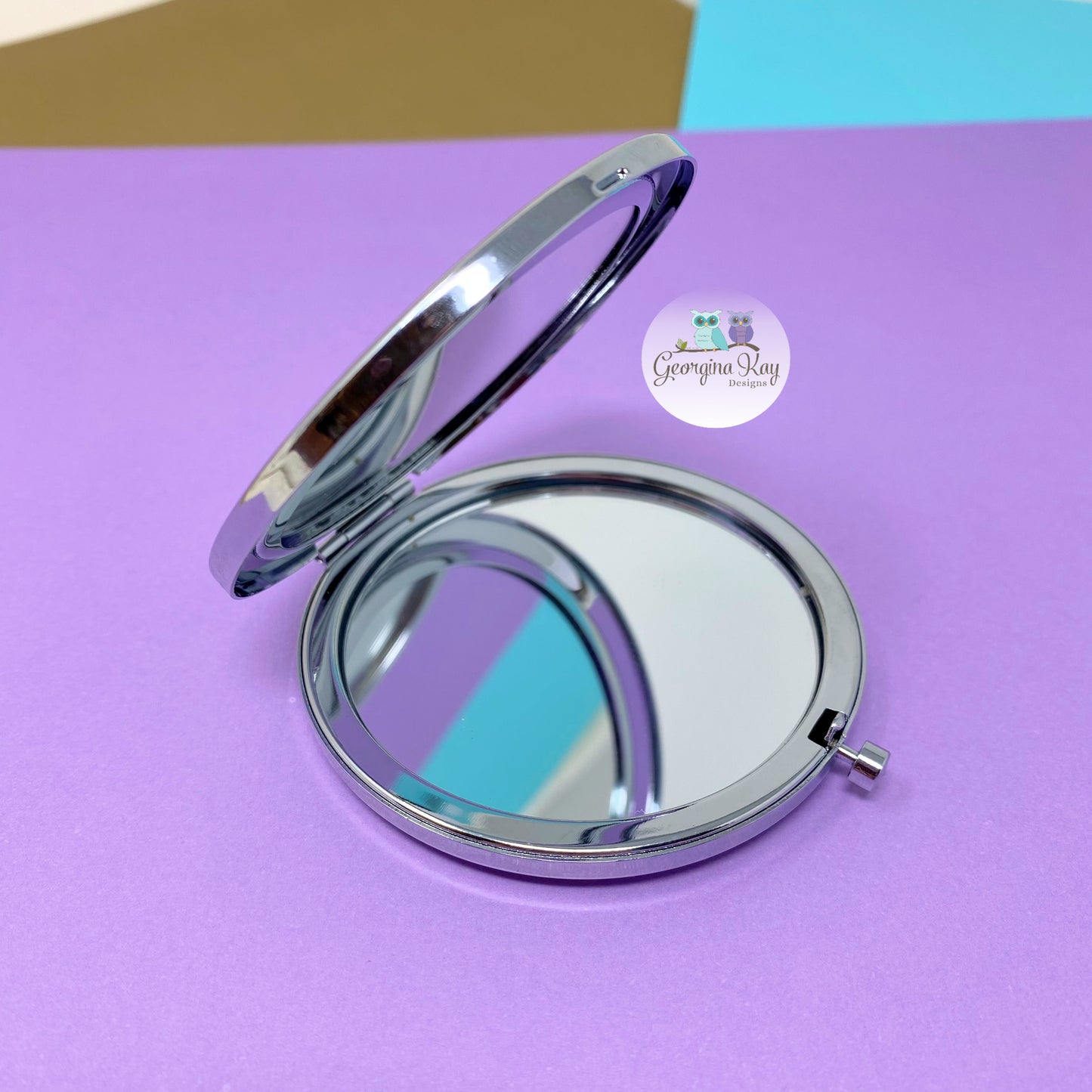 Compact mirror on a purple background with a brand logo in the corner.