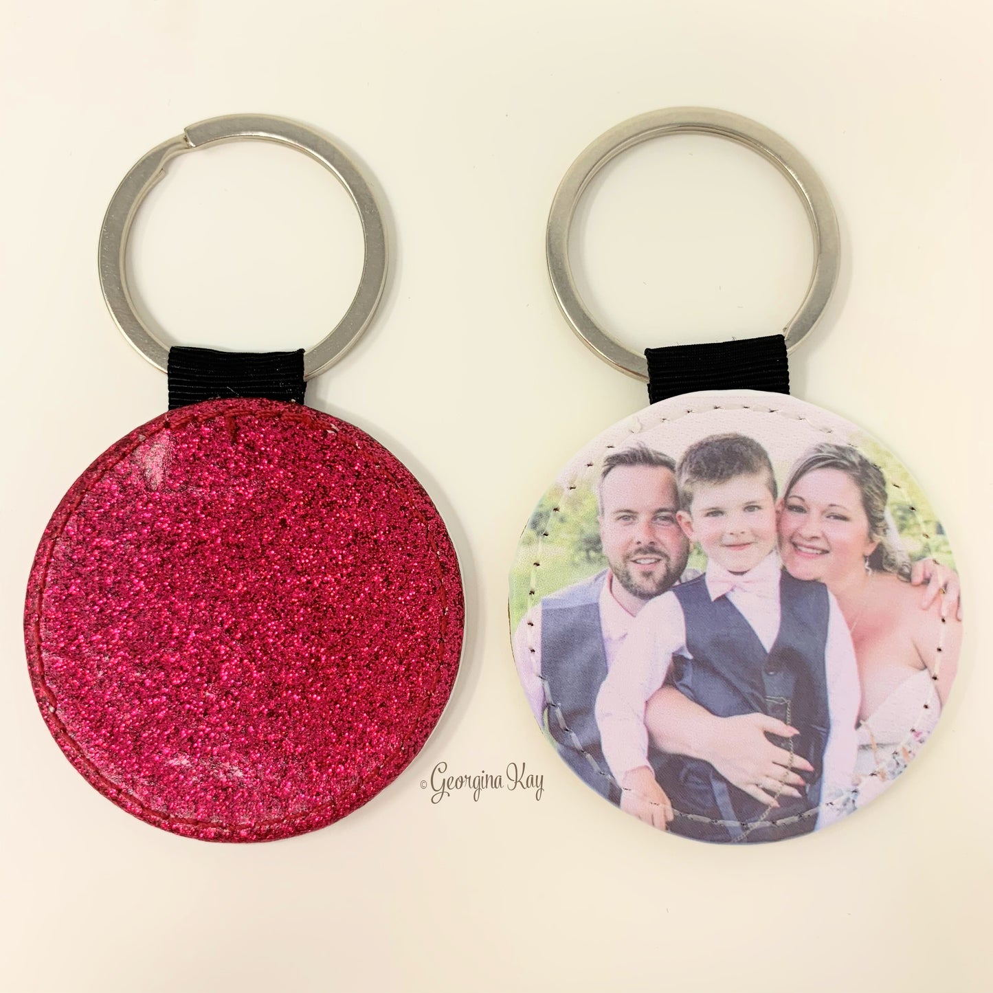 Two keychains, one pink glittery and one with a photo of a family, on a light beige background.
