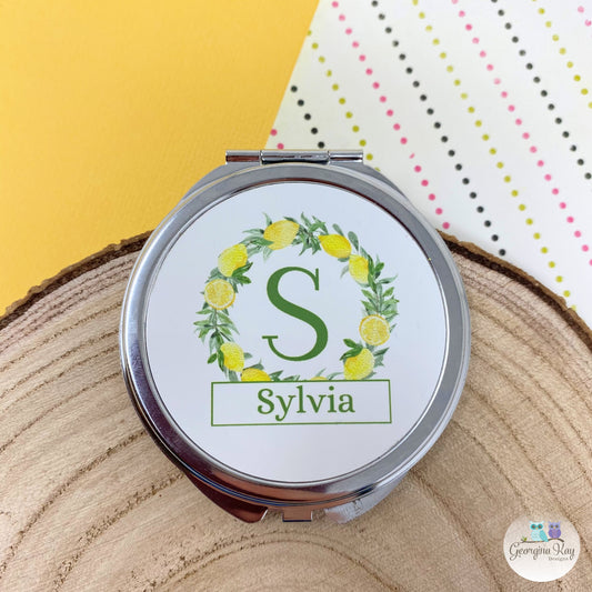 Compact mirror with 'S' and 'Sylvia' design on a wooden surface with polka dot background
