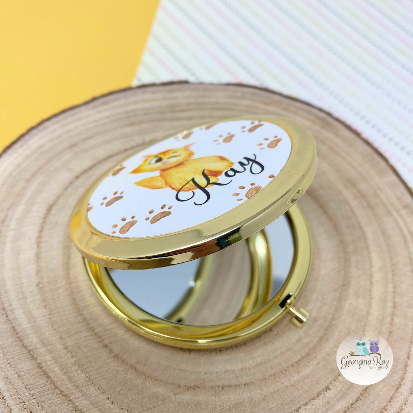 Compact mirror with a gold frame featuring a cartoon fox design on a wooden surface.