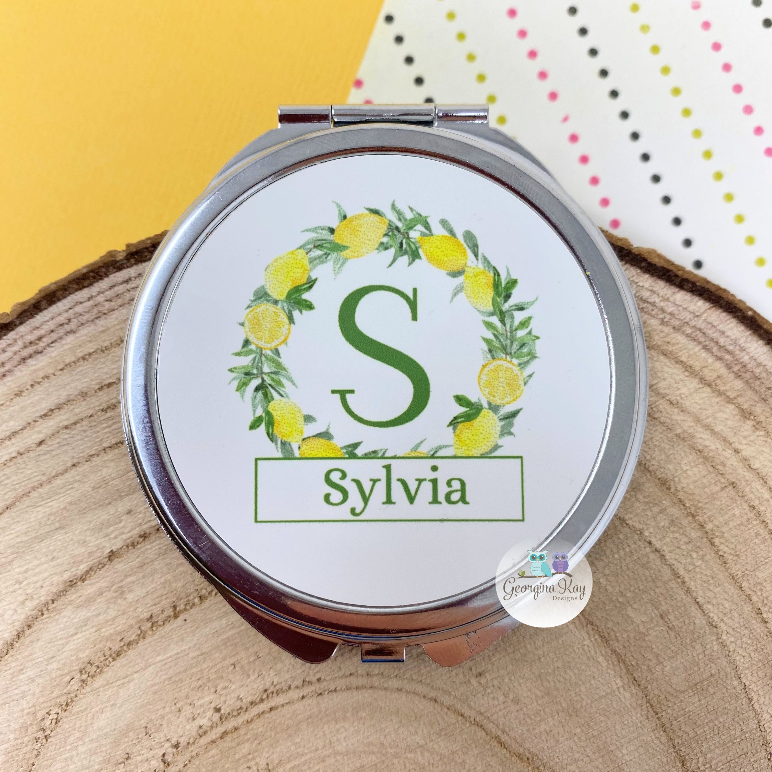 Compact mirror with floral design and name 'Sylvia' on a wooden surface